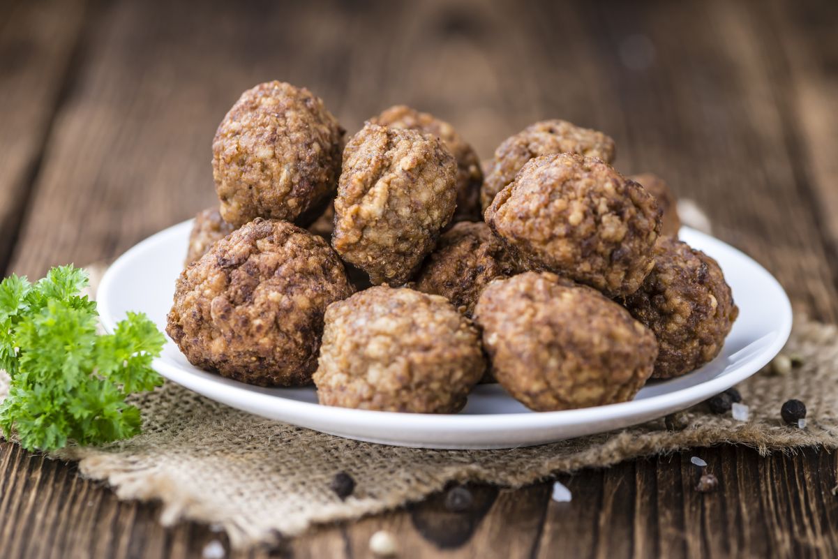 A pile of Simple Weight Watchers Italian Meatballs on a white plate, sitting on a piece of burlap, on a dark rustic wood surface.