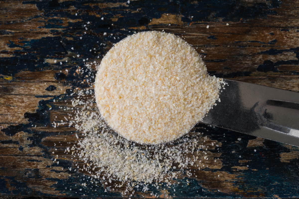 Onion powder in a measuring spoon sitting on a dark, rustic surface.