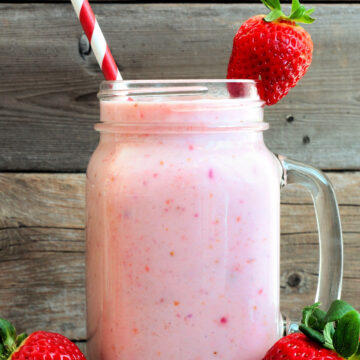 Weight Watchers Strawberry Vanilla Protein Shake Recipe in a clear glass with a striped straw, on a rustic surface with fresh strawberries around it.