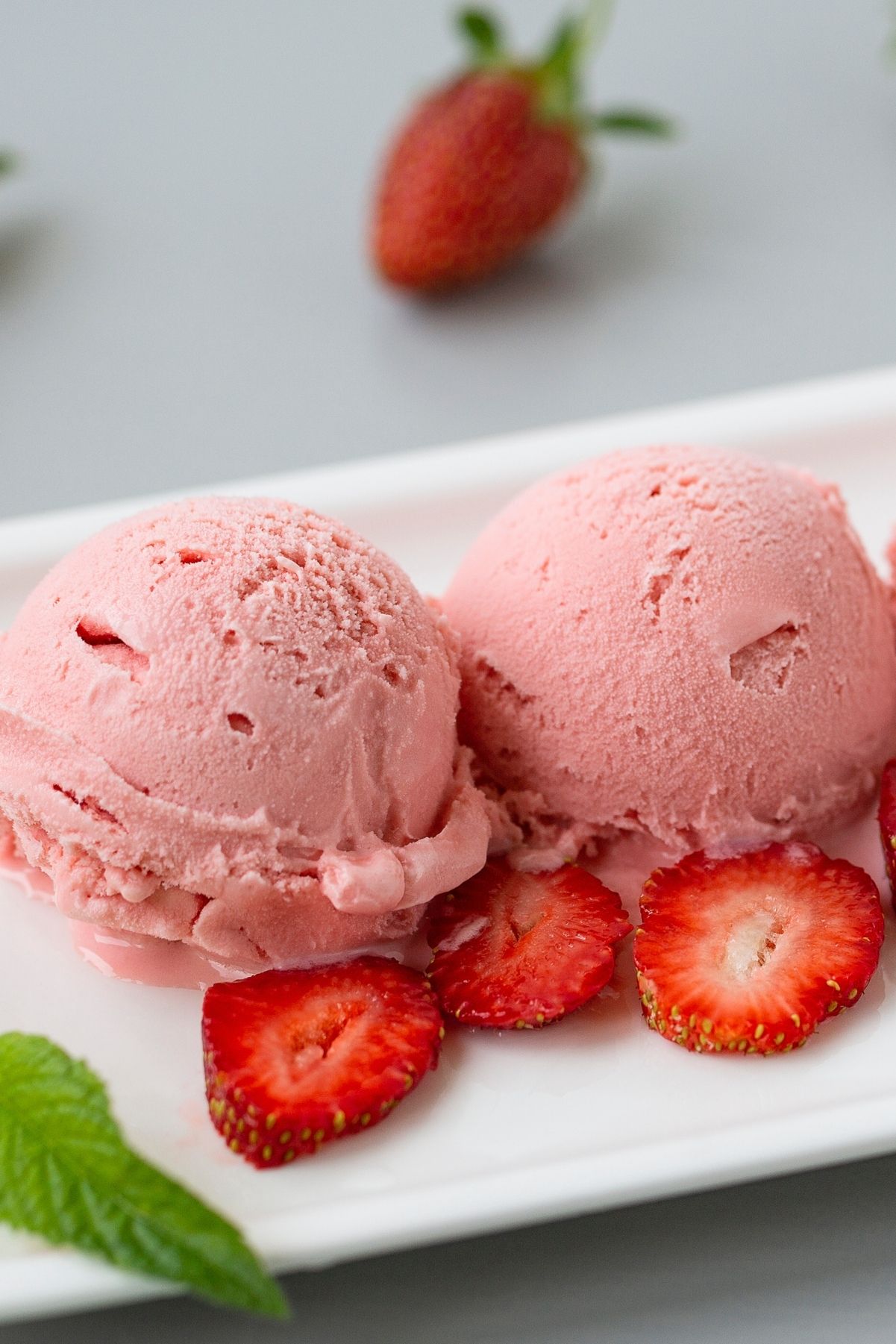 2 scoops of Homemade Strawberry Sherbet on a white plate with fresh strawberries.