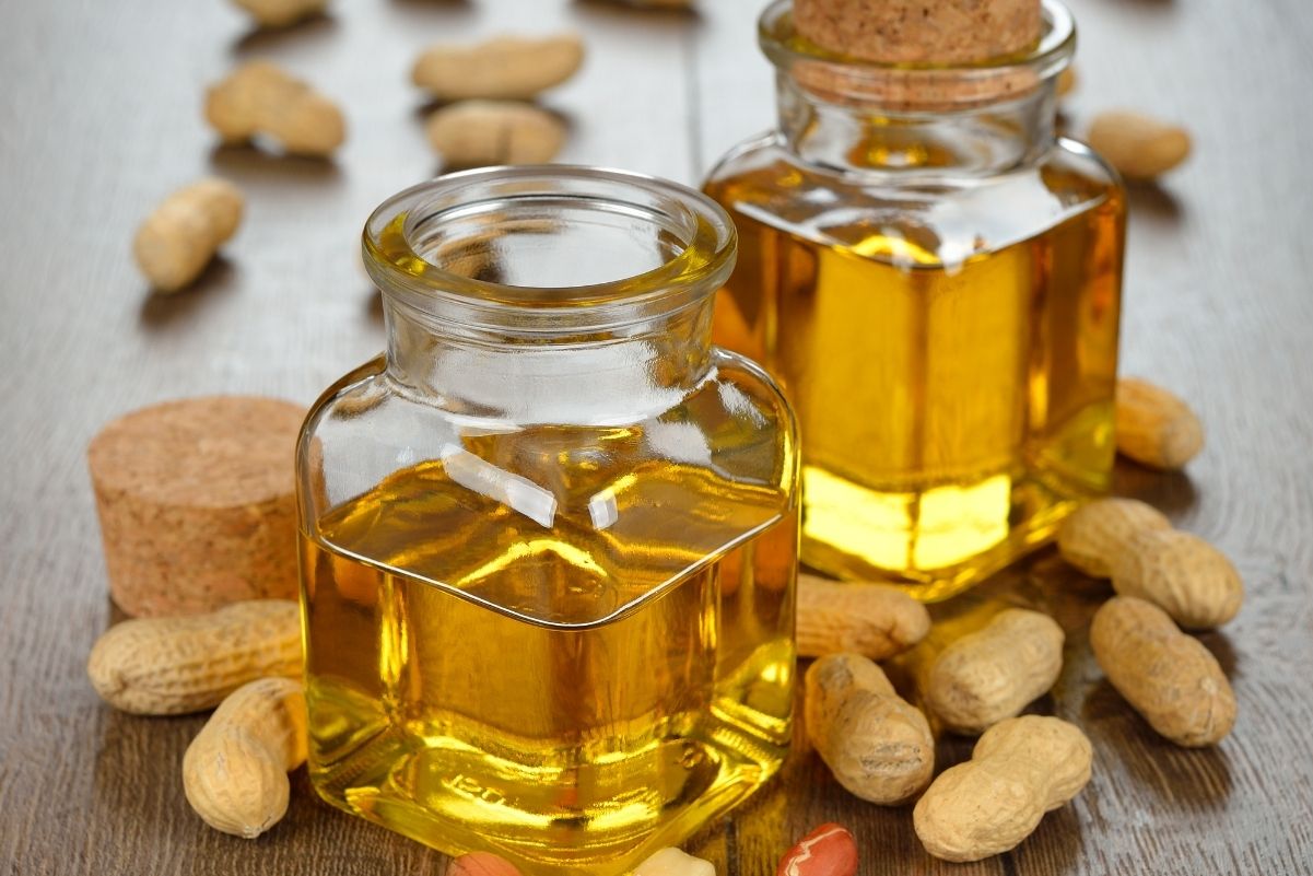 Peanut oil in clear glass jars with shelled peanuts around them.