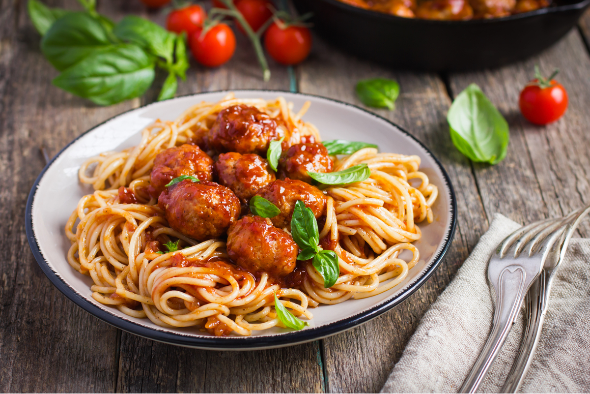Simple Weight Watchers Spaghetti and Meatballs on a white plate with a black trim on a rustic wooden surface with flatware on a napkin next to it.