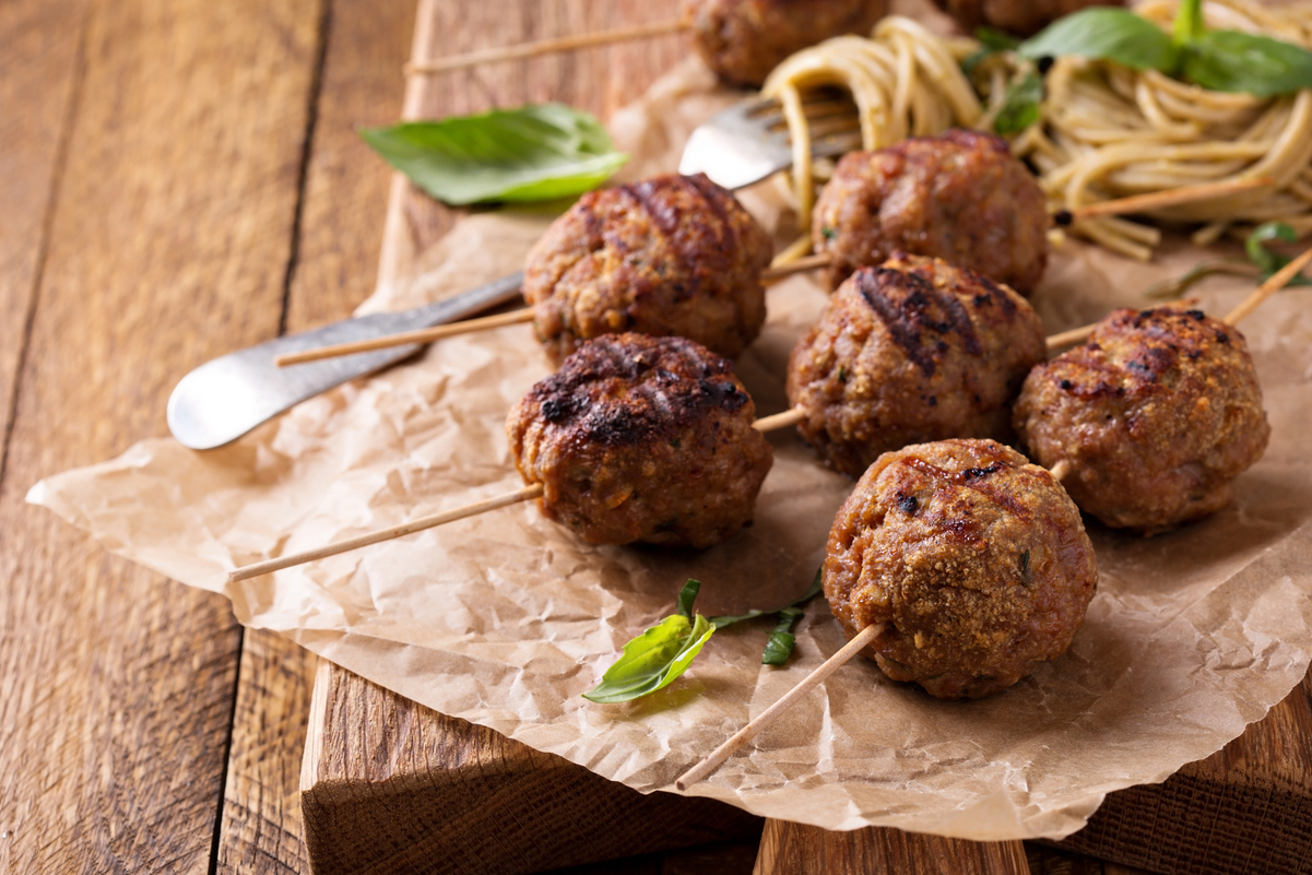 6 Weight Watchers Ground Turkey Pesto Meatballs on wooden skewers with spaghetti out of focus in the background.