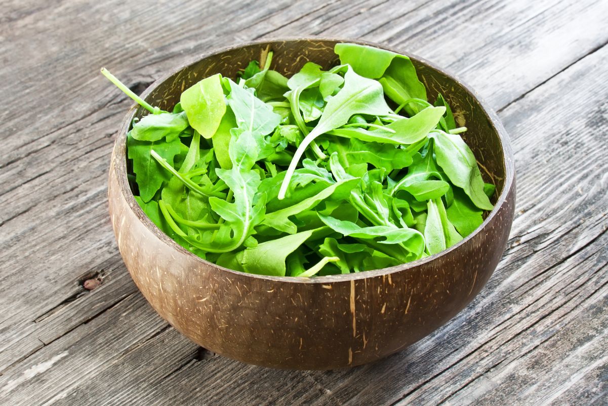 Fresh Arugula in a wooden bowl on a rustic surface.