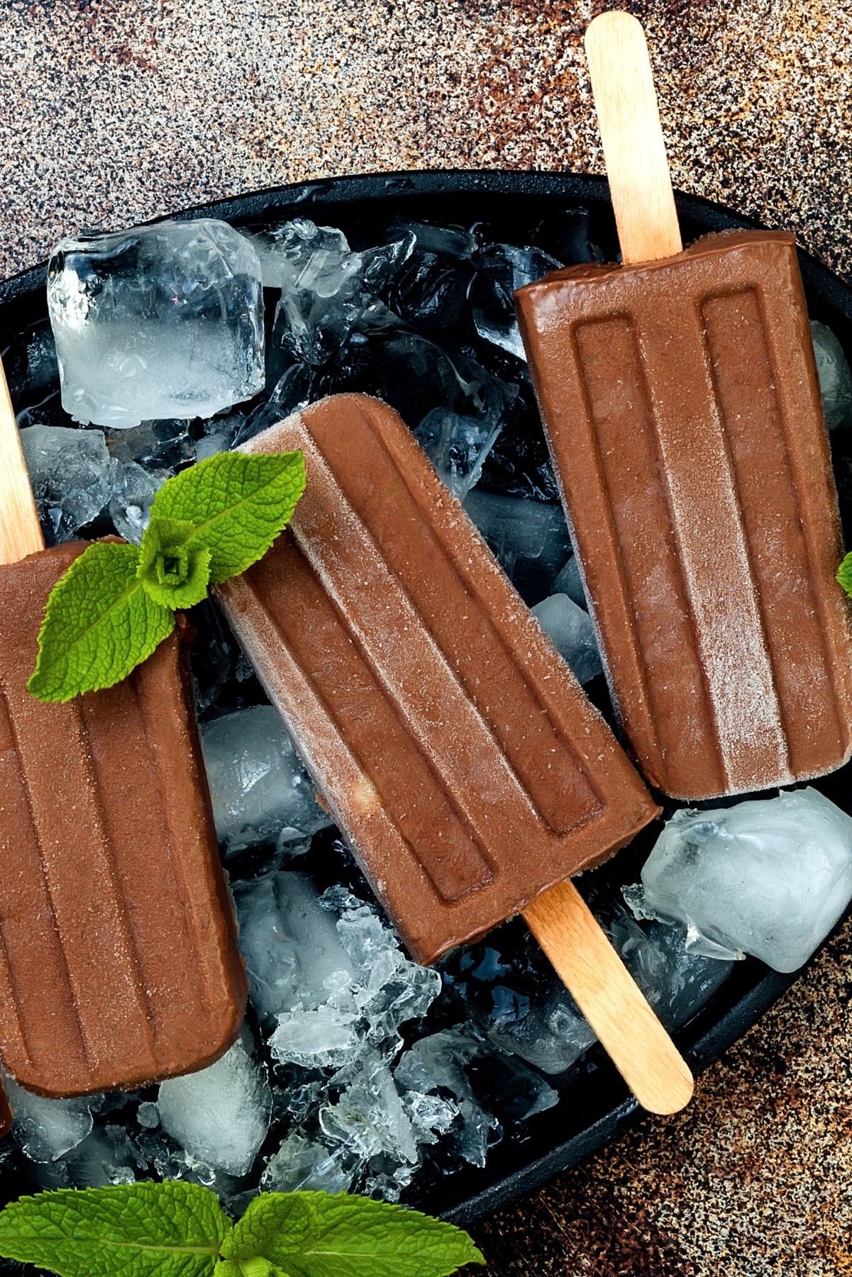 3 Homemade Weight Watchers Fudge Popsicles on a black plate with ice cubes.