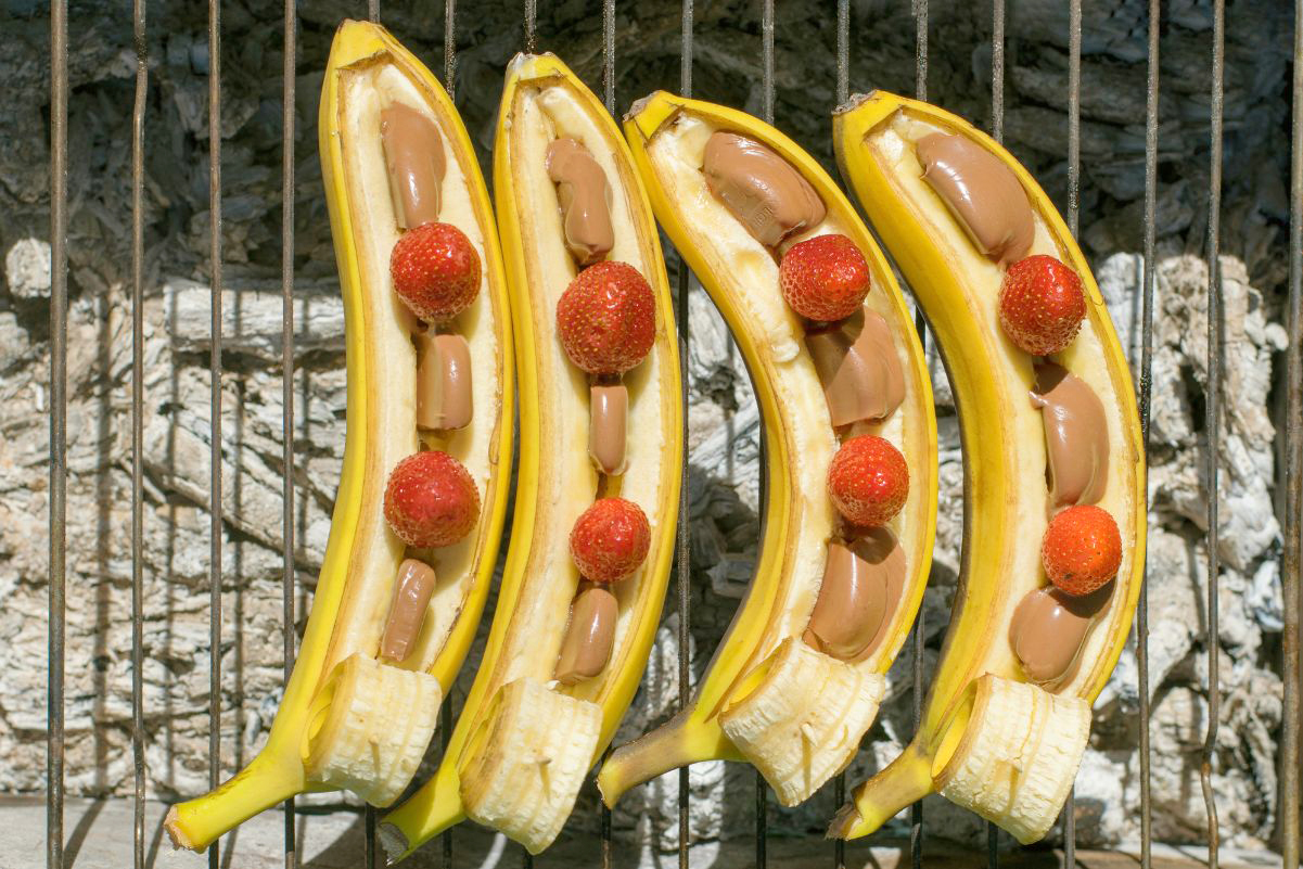 4 Grilled Bananas stuffed with Chocolate and Strawberries on a grill.