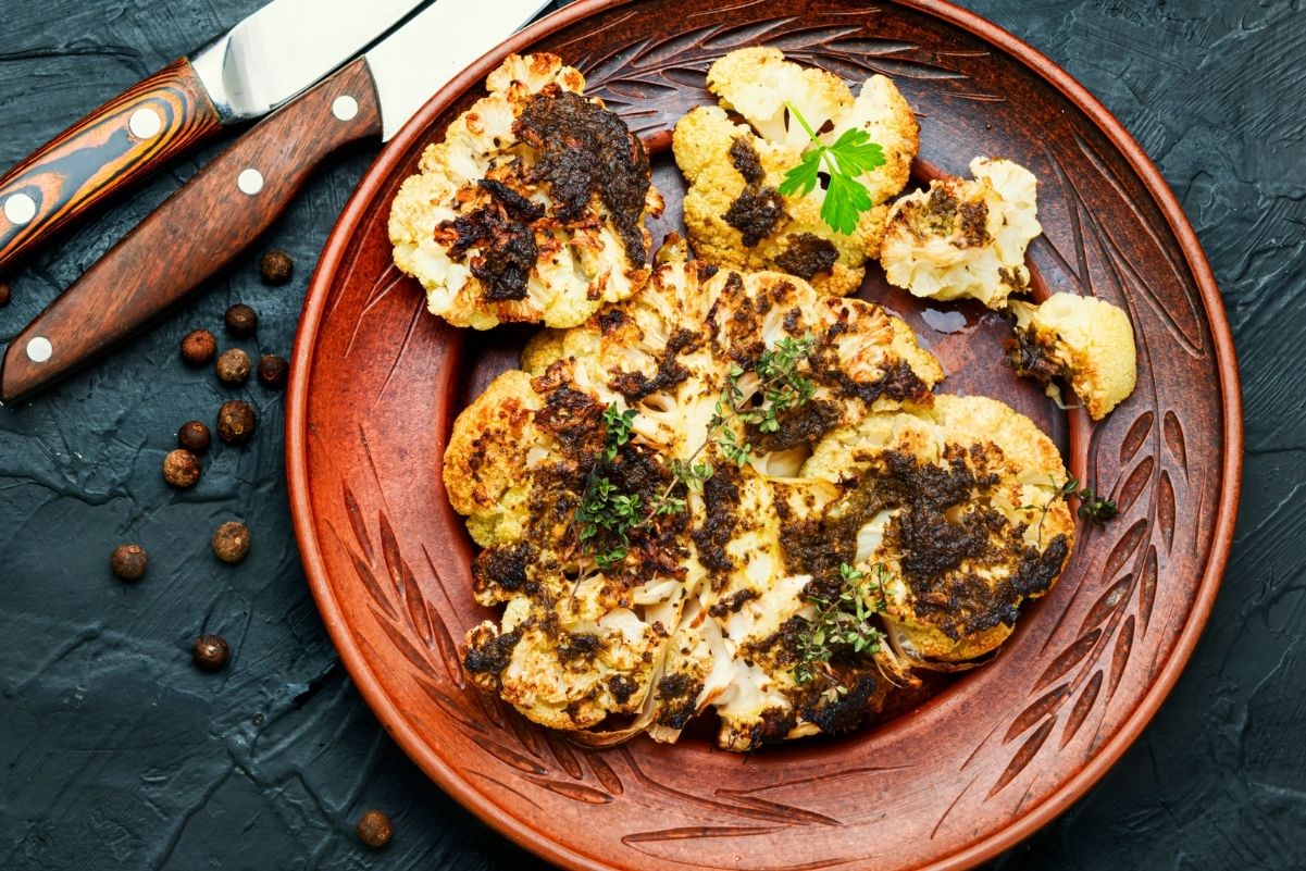 Weight Watchers Grilled Pesto Cauliflower Steaks Recipe on a brown plate with 2 steak knives next to it.