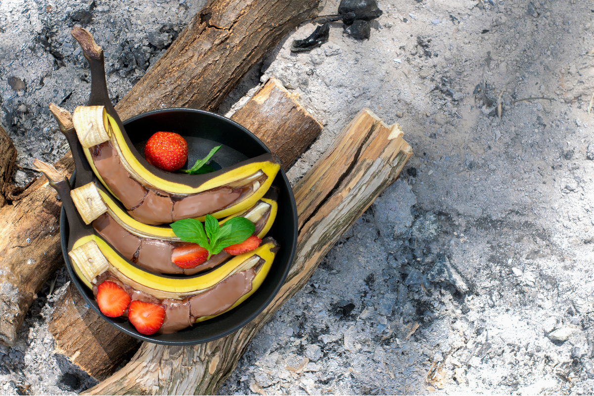 3 Grilled Bananas with Chocolate and Strawberries on a stack of wood.