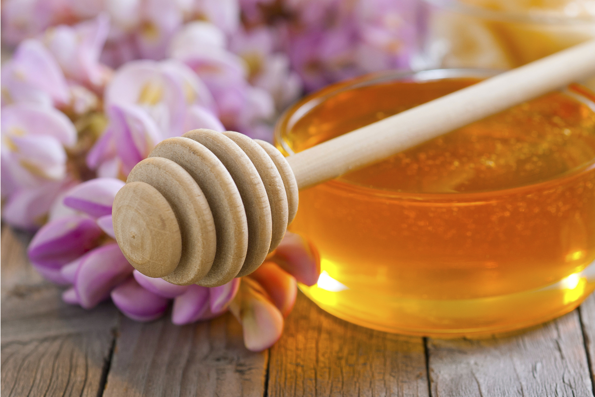 Honey in a clear glass jar with a honey dipper sitting on top.