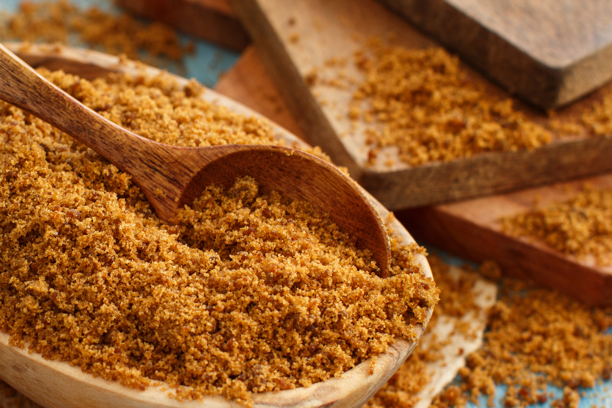 Brown sugar in a wooden bowl with a wooden spoon in it.