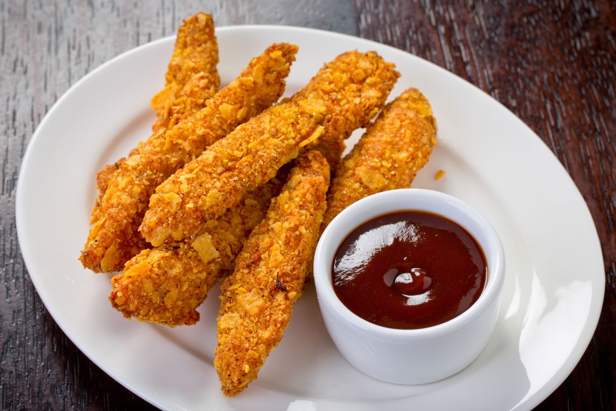 Weight Watchers Chicken Fingers on a white plate with a small ramekin of barbecue sauce on a wooden surface.