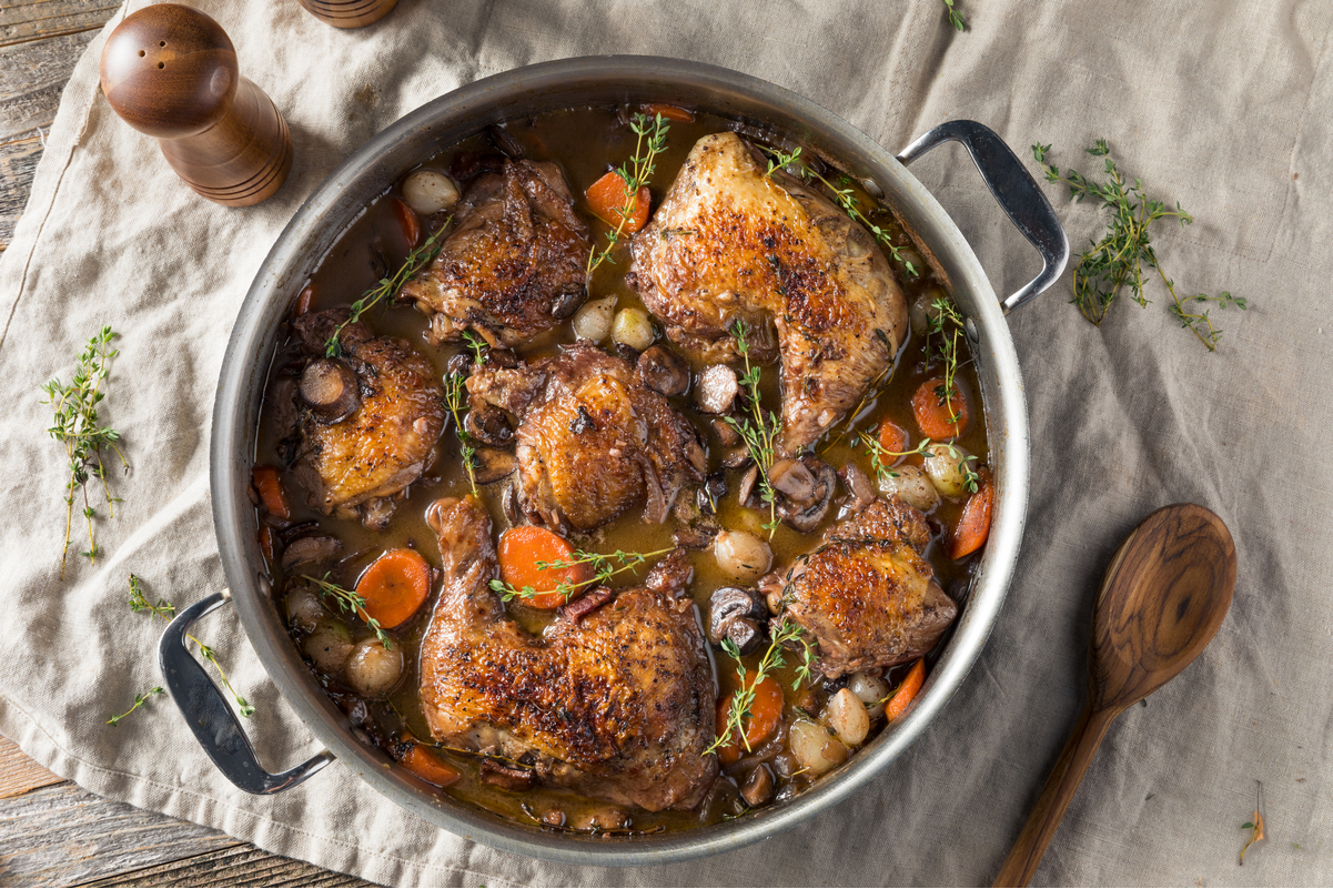 Overhead view of Best Weight Watchers Coq Au Vin in a silver pot, sitting on a linen fabric with a wooden spoon next to it.