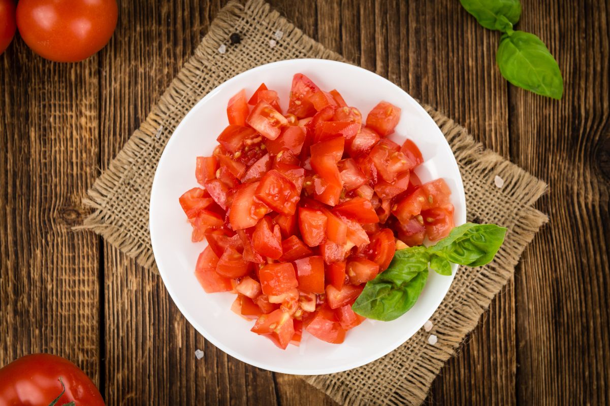 Diced tomatoes on a white dish sitting on a piece of burlap on a dark wooden table.