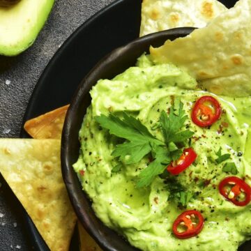 Closeup of overhead view of Simple Weight Watchers Whipped Guacamole in a black bowl on top of a black plate with tortilla chips on it.