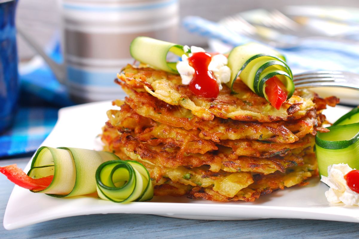 A stack of Weight Watchers Zucchini Potato Pancakes with zucchini ribbons around it. Sitting on a white plate with a colorful background.