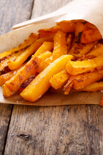 Closeup of Easy Weight Watchers Baked Butternut Squash Fries wrapped in paper, sitting on a rustic surface.