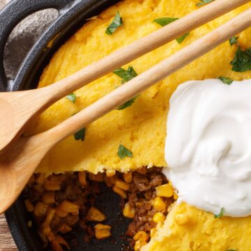 Weight Watchers Turkey Tamale Casserole on a black pan with wooden spoons on top of it.