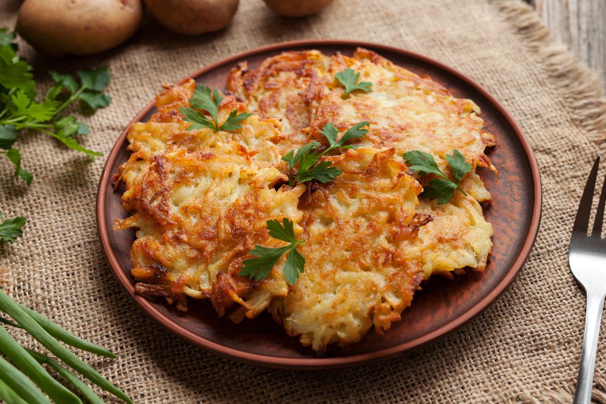 Weight Watchers Air Fryer Latkes (Potato Pancakes) on a round, brown, plate on a wooden table with raw potatoes behind it.