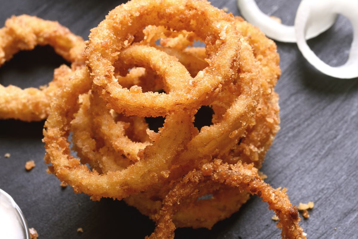 Closeup of a pile of Air Fryer Weight Watchers Onion Rings on a dark slate surface.