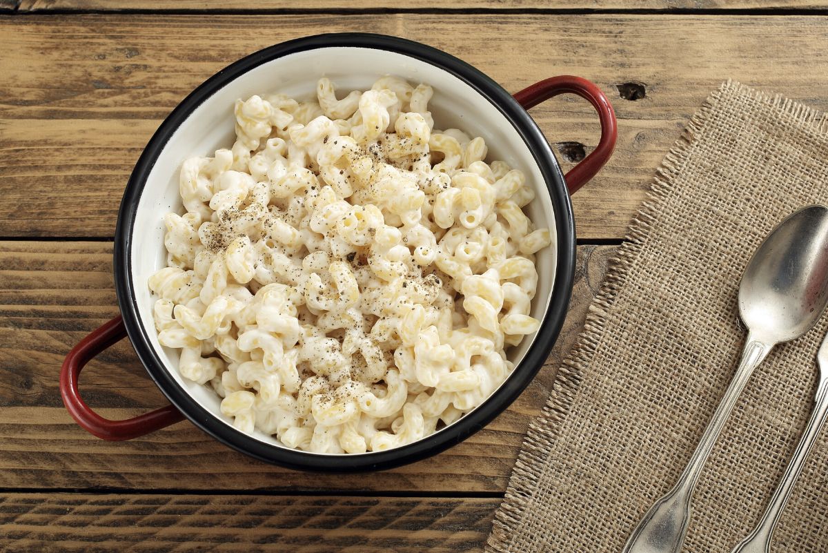 Over head view of Weight Watchers Alfredo Macaroni in a red pot on a rustic wooden surface with a piece of burlap next to it.