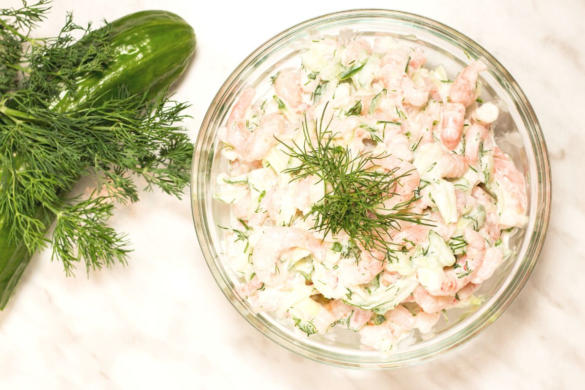 Overhead view of Weight Watchers Dill Shrimp Salad Sandwich with Cucumber in a clear glass bowl, a cucumber and fresh dill next to it.