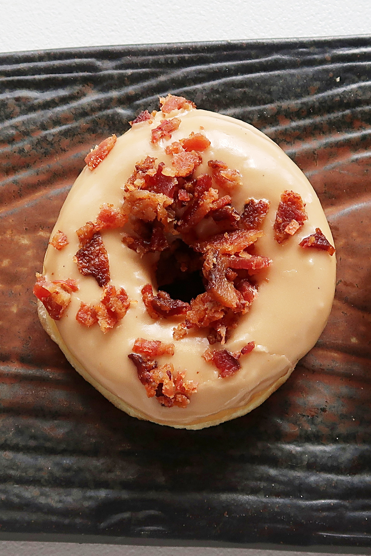 Closeup of a Weight Watchers Maple Glazed Doughnuts with Bacon on a rustic wood surface.