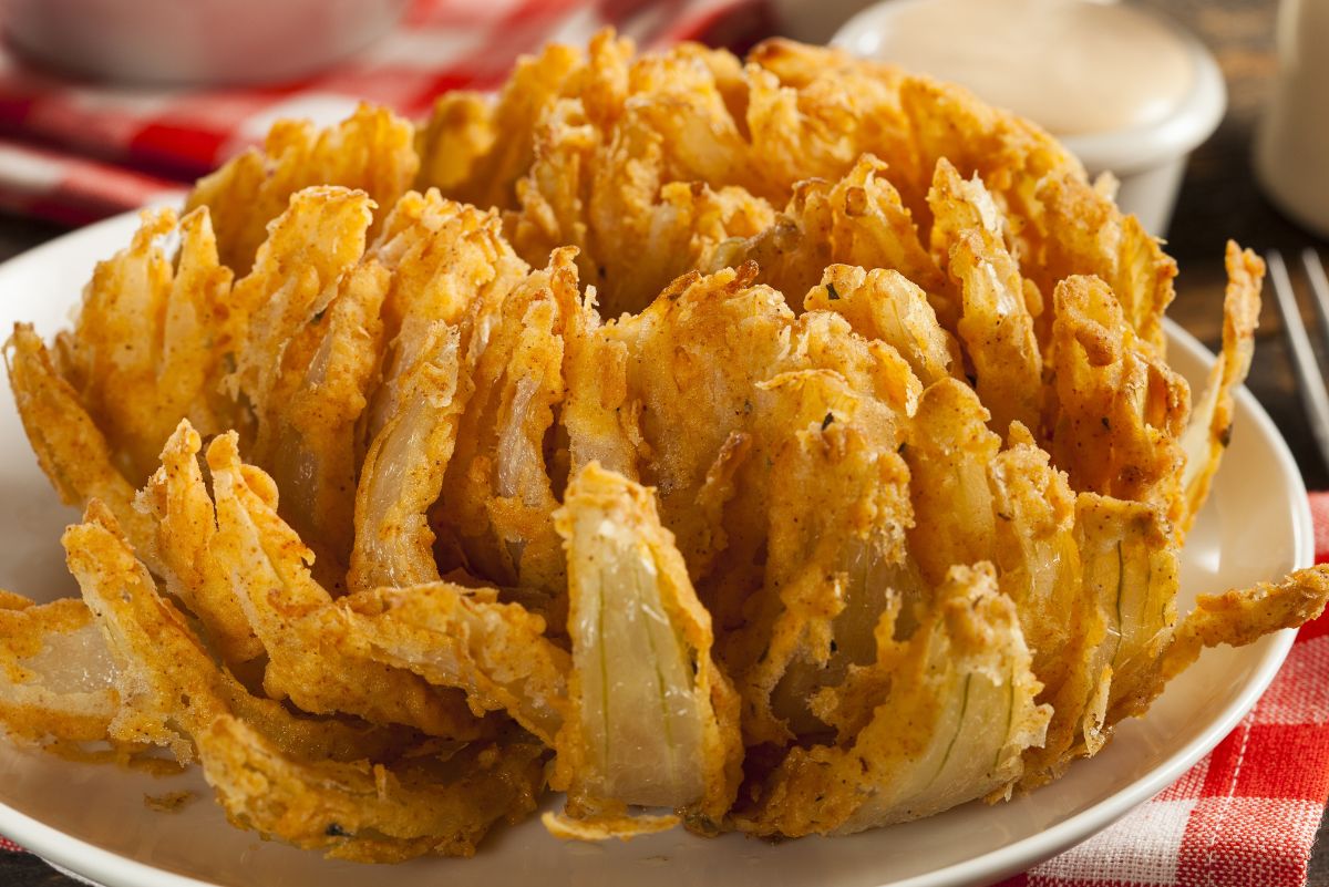 Low Calorie Air Fryer Blooming Onion on a white plate sitting on a red and white checked tablecloth.