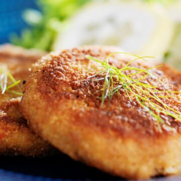 2 Weight Watchers Maryland Crab Cakes on a blue plate with an out of focus lemon slice in the background.