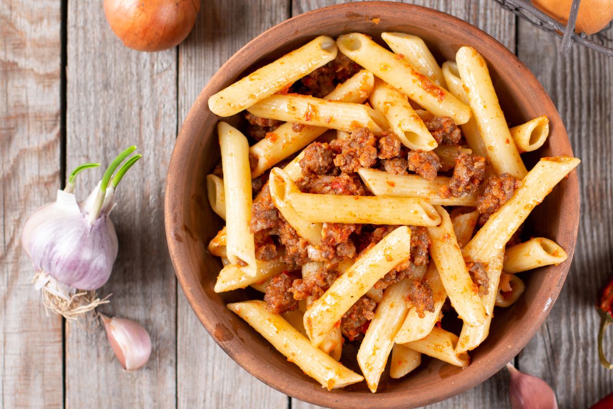 Overhead view of Weight Watchers Penne Pasta with Meat Sauce in a brown bowl on a rustic, wooden surface.