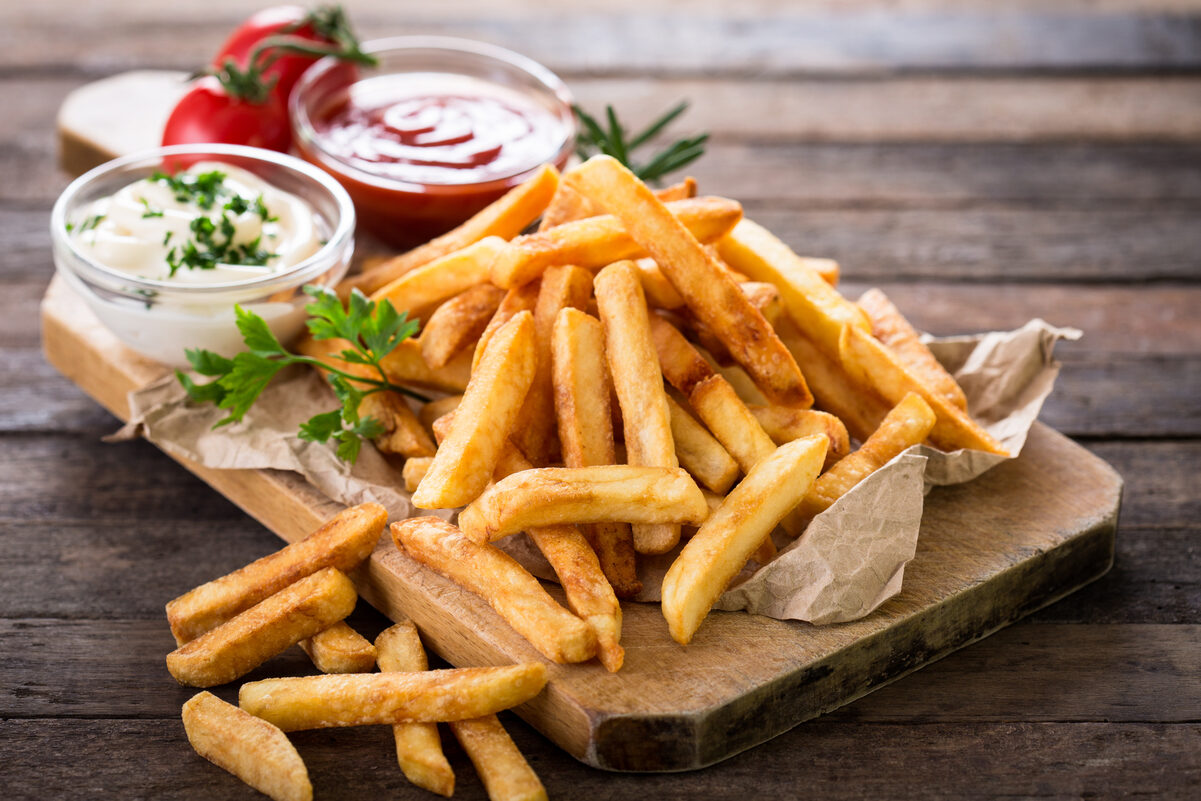 Weight Watchers Baked Garlic & Herb Fries on a wooden cutting board with small bowls of condiments.