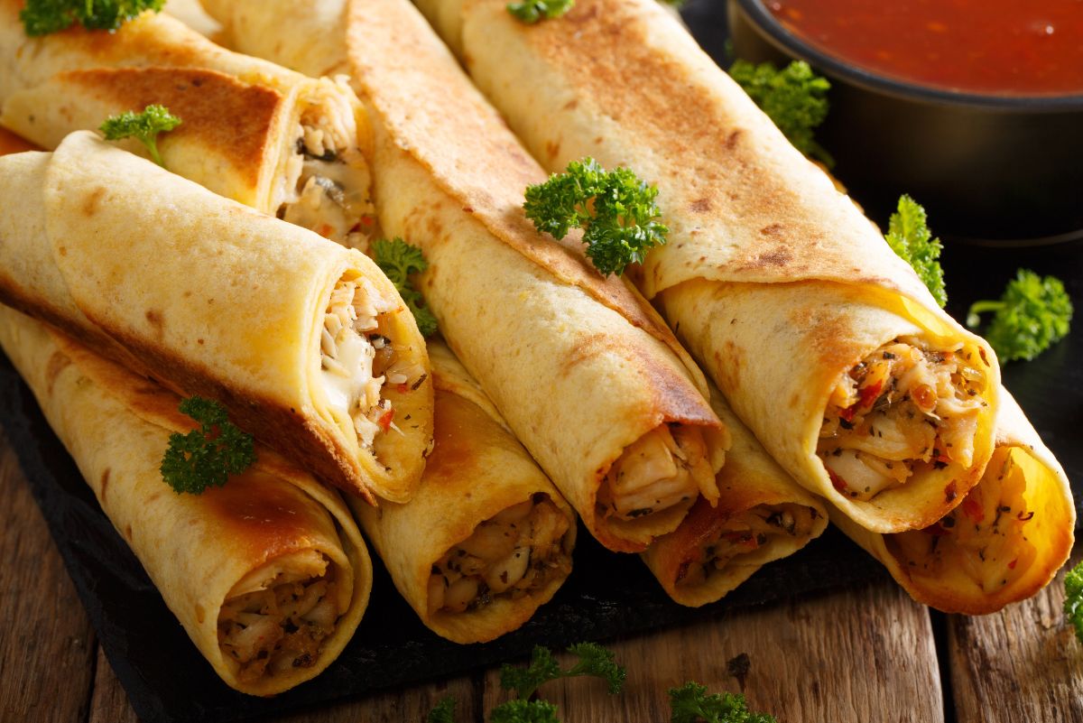 A pile of Quick Mexican Chicken Taquitos (Air Fryer) on a rustic wooden surface.