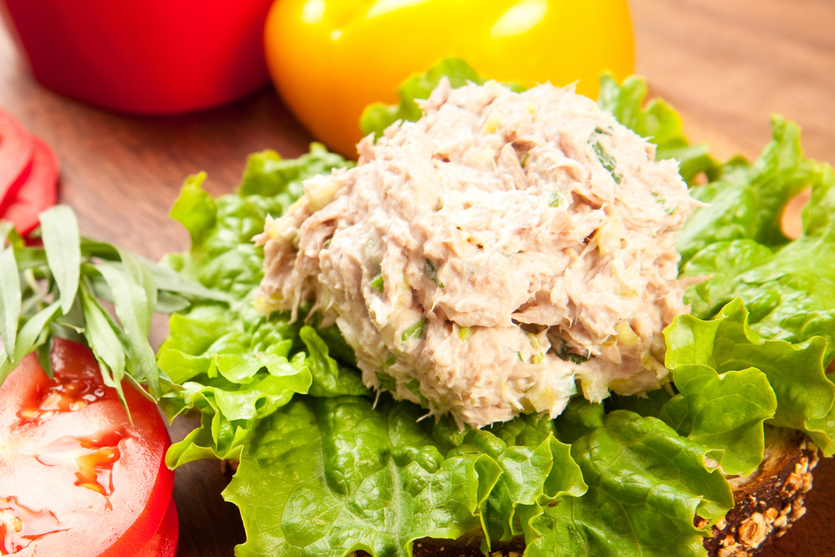 A scoop of tuna salad on a bed of lettuce, surrounded by tomatoes, red, and yellow bell peppers.