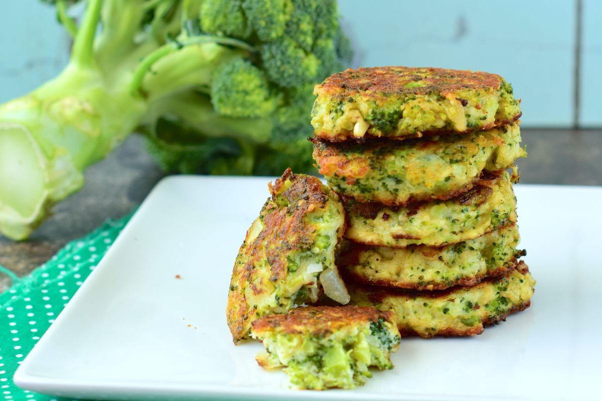 A stack of Weight Watchers Cheesy Broccoli Fritters on a white cutting board with fresh broccoli behind it.