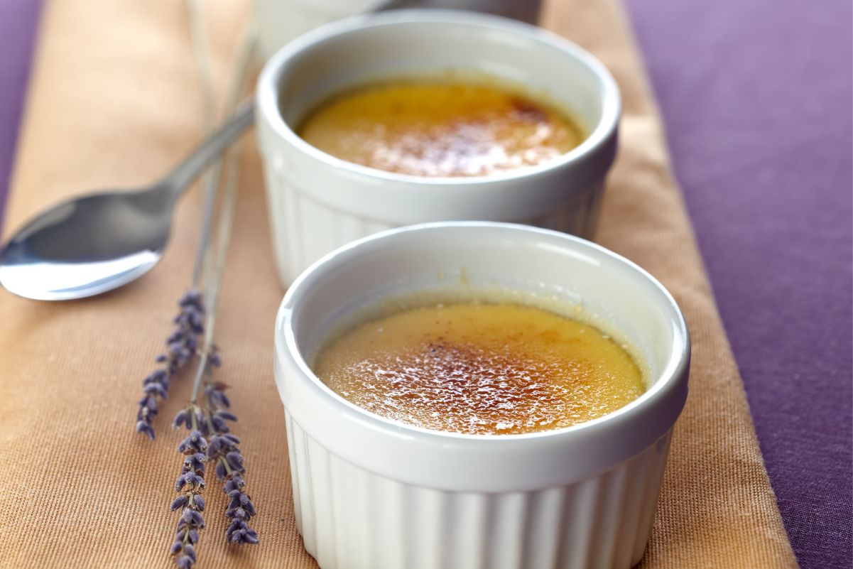 3 Weight Watchers Lavender Creme Brulee in white ramekins on a cutting board with fresh lavender next to them.