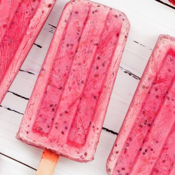 Closeup of 3 Weight Watchers Raspberry Yogurt Popsicles with a few fresh raspberries around them.