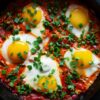 Closeup of Shakshouka (Eggs with a Twist) in a black iron skillet.