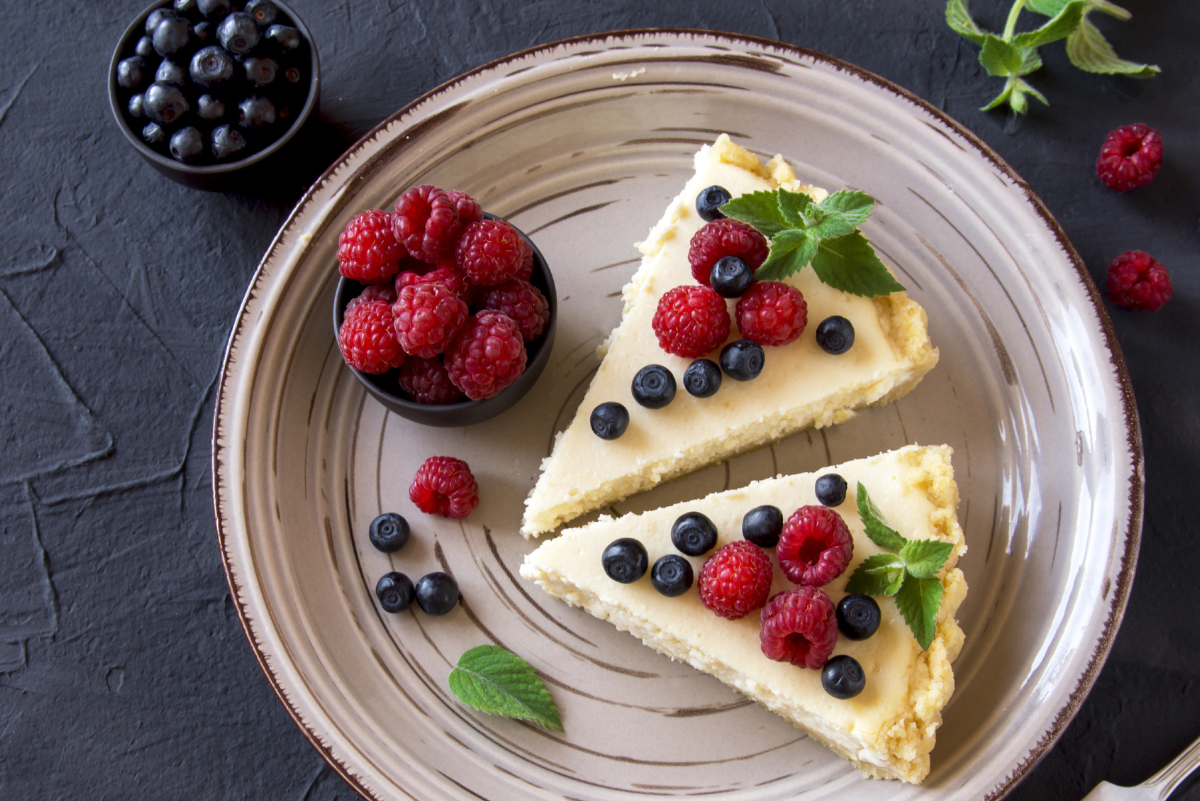 Overhead view of 2 slices of Weight Watchers Berry Cheesecake Pie on a white plate with fresh raspberries and blueberries.