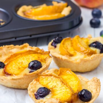 Homemade Weight Watchers Individual Peach Pies with a pan behind them. Fresh peaches and blueberries in the background.