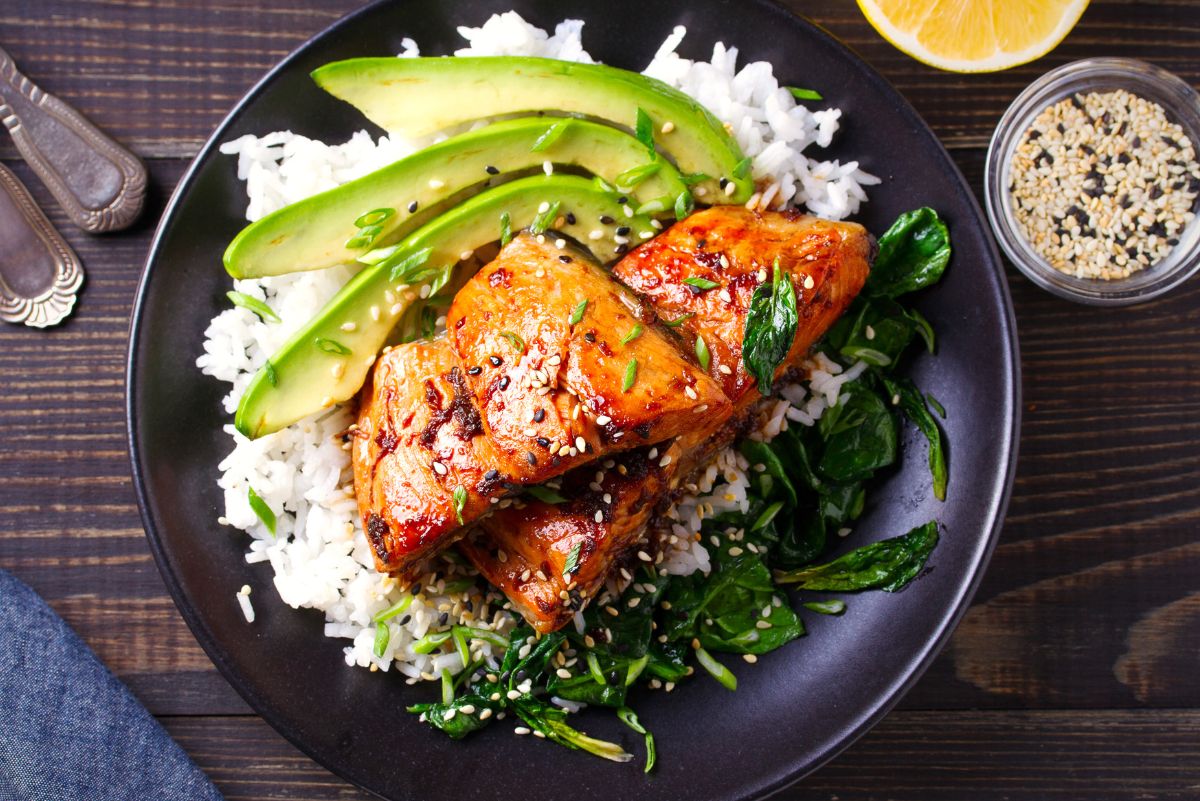 Weight Watchers Spicy Grilled Salmon with Sesame Sauce on a black plate with rice and sliced avocado.