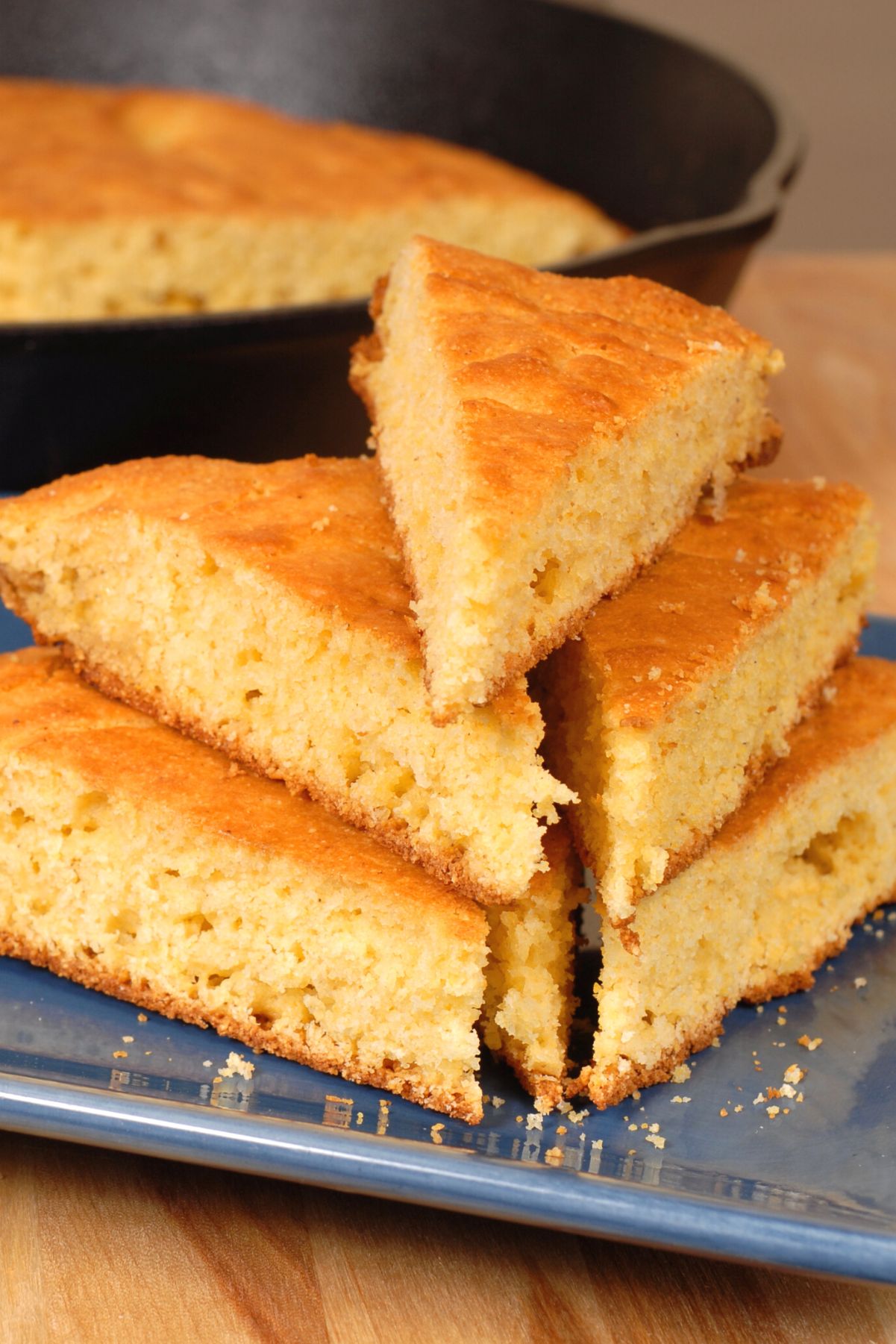 Sliced Homemade Cornbread stacked on a blue plate with a black pan in the background.