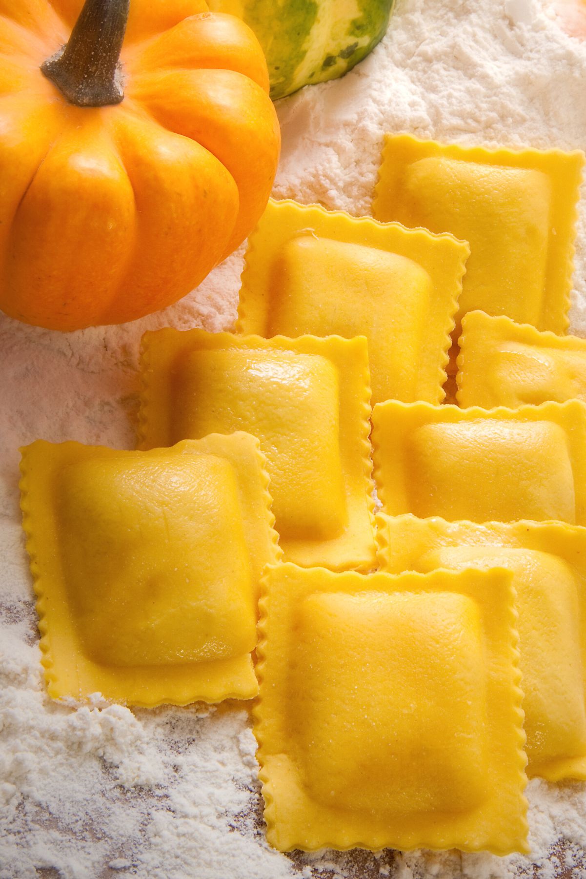 Weight Watchers Homemade Pumpkin Ravioli with loose flour scattered around and a fresh pumpkin next to it.