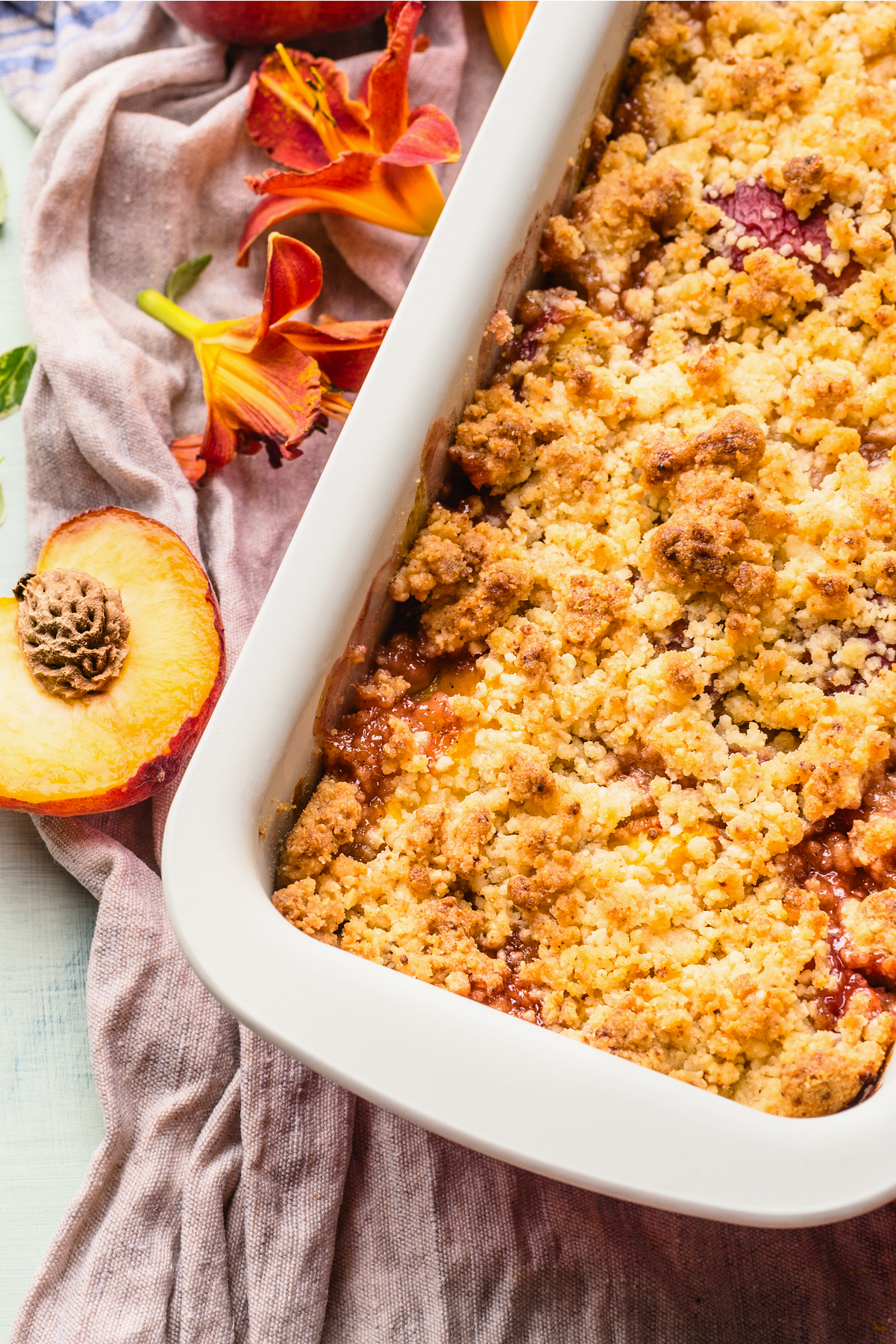 Closeup, overhead view of Weight Watchers Easy Peach Crumble in a white baking dish with a fresh, cut peach next to it.