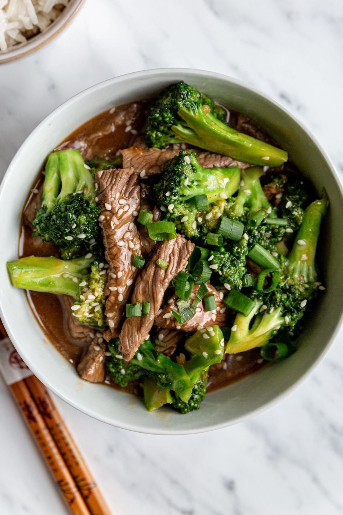 Overhead view of Weight Watchers Spicy Beef and Broccoli in a white bowl with chopsticks next to it.