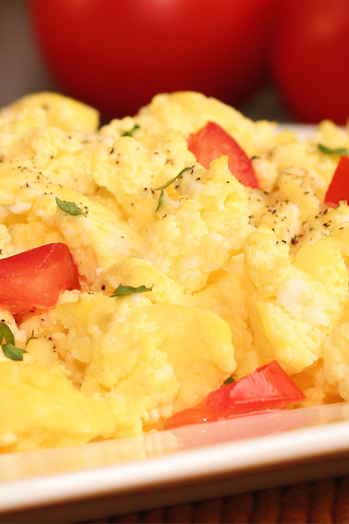 Closeup of Weight Watchers Scrambled Eggs with Tomatoes breakfast on a white plate with fresh tomatoes in the background.