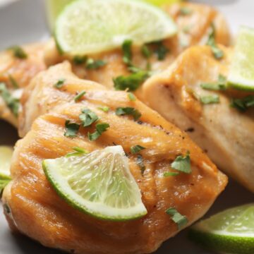 A plate featuring broiled ginger and lime chicken garnished with cilantro and lime wedges, showcasing a golden-brown glaze on the chicken's surface with a focus on the vibrant, fresh garnishes.