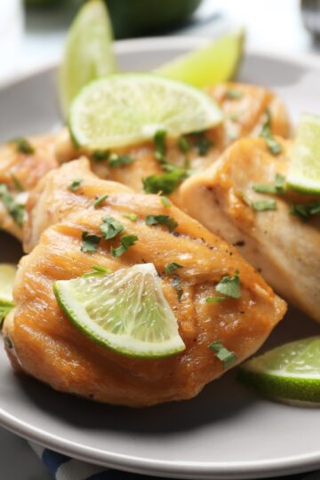 A plate featuring broiled ginger and lime chicken garnished with cilantro and lime wedges, showcasing a golden-brown glaze on the chicken's surface with a focus on the vibrant, fresh garnishes.