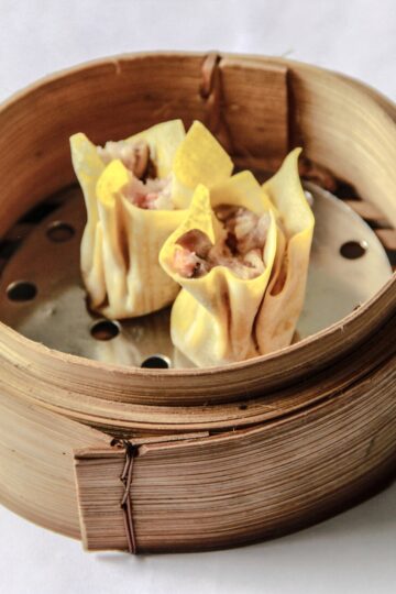 Close-up view of ginger pork shiitake dumplings in a bamboo steamer, highlighting the filling and the folded wonton wrappers.