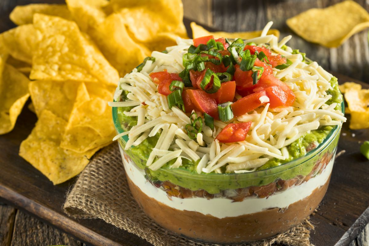 Individual Mexican Layer Dip in a glass bowl surrounded by tortilla chips.