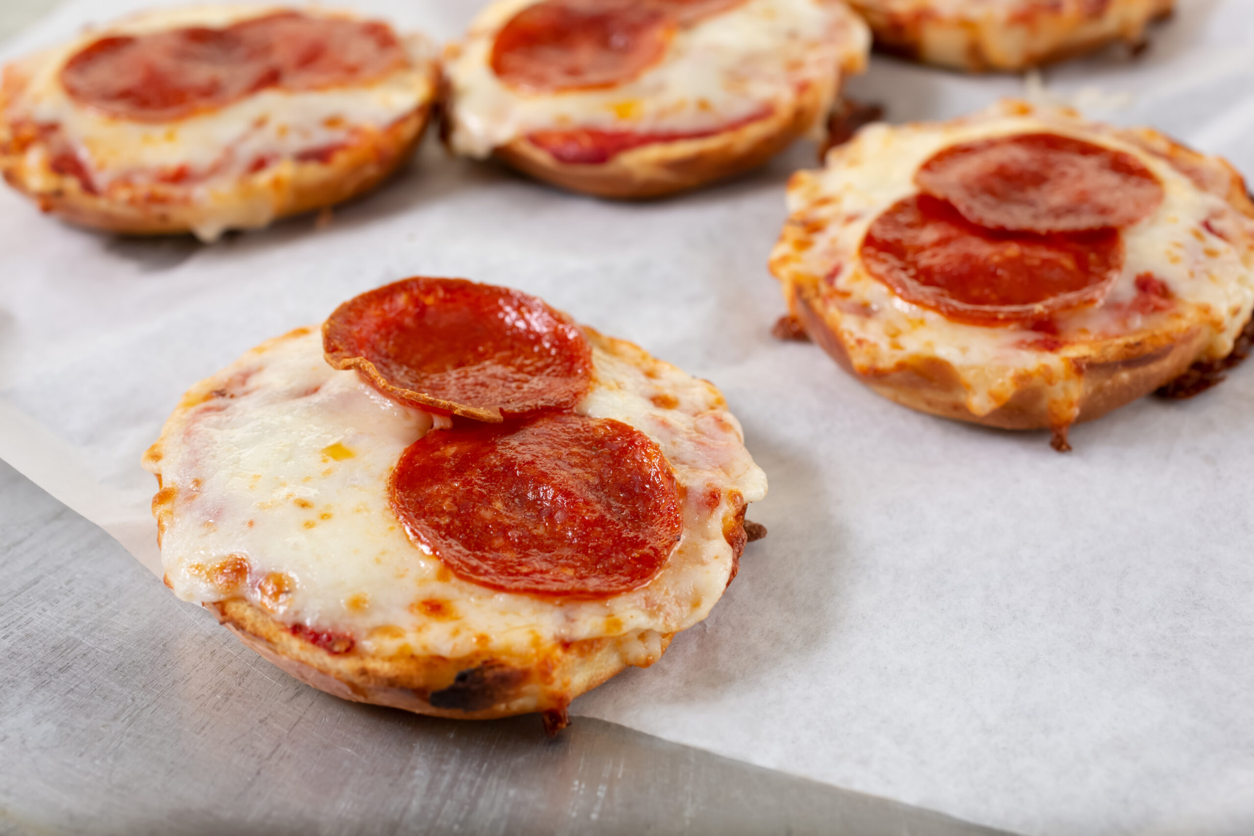 Pizza Bagel Bites on parchment paper sitting on a silver colored metal surface.