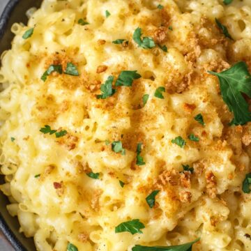 Close-up view of Healthier Bacon Macaroni and Cheese in a black cast iron skillet, garnished with chopped parsley on top, indicating a crispy breadcrumb topping and a creamy cheese sauce.